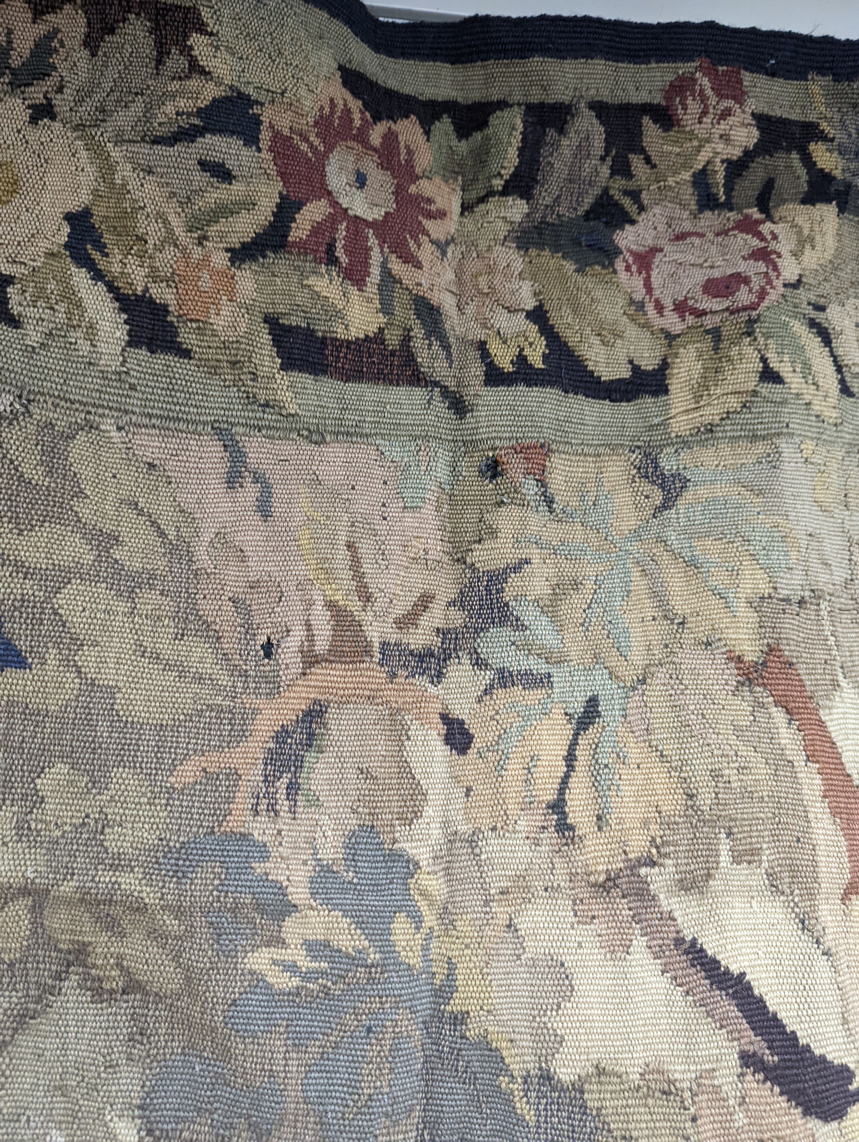 A late 19th / early 20th century French tapestry depicting a woodland scene with trees and flowers with a floral border woven in autumnal colours